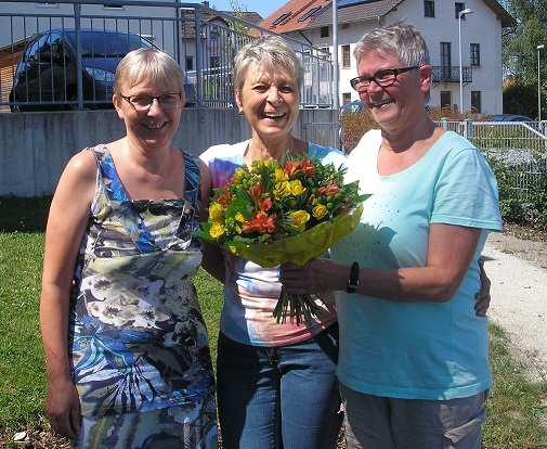 Brigitte Graßer (rechts) überreicht an Johanna Krzywania (Mitte) einen Blumenstrauß. Links im Bild K
